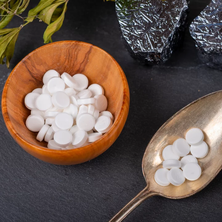 Weiße Schüßler-Salze-Tabletten in einer Holzschale und auf einem antiken Löffel